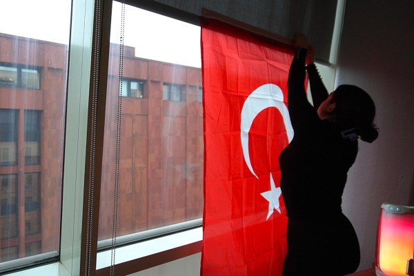 A woman hanging a Turkish flag on a curtain by a window at N.Y.U.'s Kimmel Center. Outside of the window is a red building.