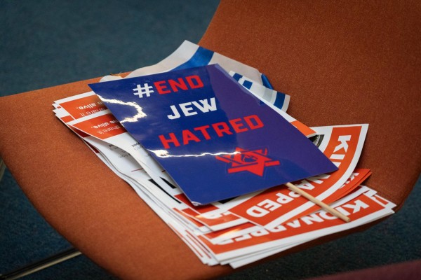 A blue poster on an orange chair with the words "#END JEW HATRED" in red and white, and a red Star of David with a blue mark of a fire at its center printed on it. Under the poster are several Israeli flags and a small stack of red and white posters with the words "KIDNAPPED" in white text.