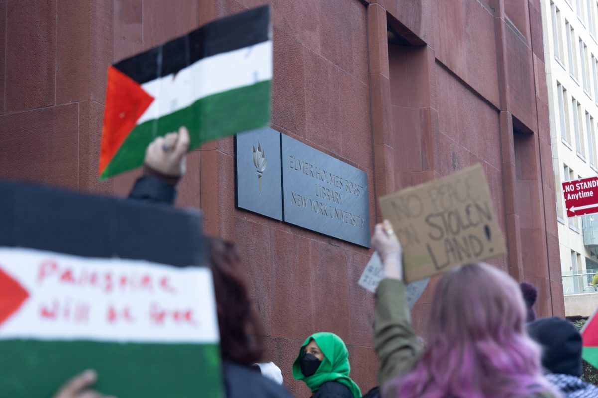 Two Palestinian flags as well as a brown sign that reads, “NO PEACE ON STOLEN LAND,” in front of Bobst Library, which is a rust-colored building.