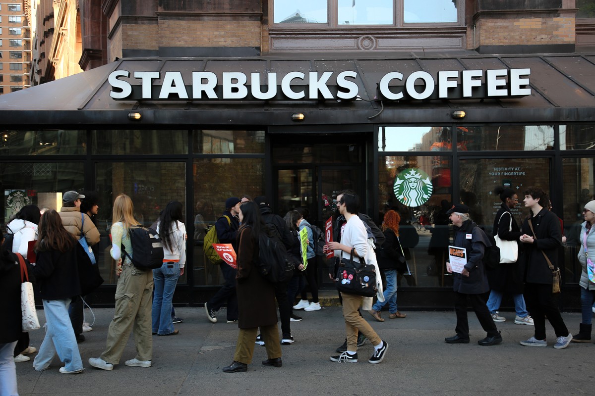 A crowd of people stands in front of a building with many windows labeled “STARBUCKS COFFEE.”