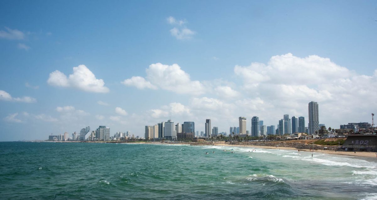 Tel Aviv seaside. There is a beach and people swimming in the sea. There are tall buildings in the background.