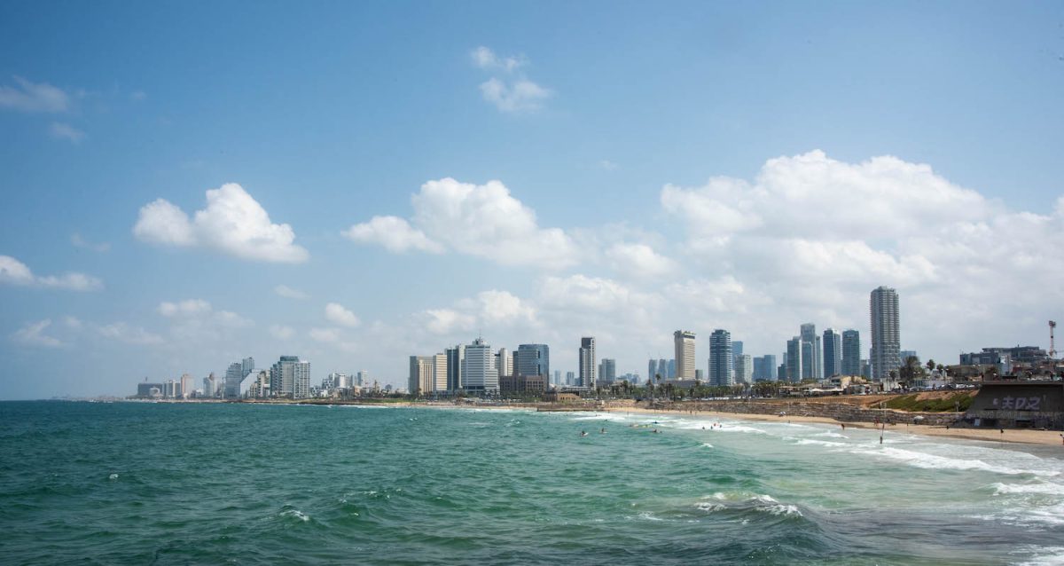 Tel+Aviv+seaside.+There+is+a+beach+and+people+swimming+in+the+sea.+There+are+tall+buildings+in+the+background.