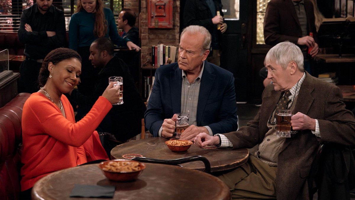 A person sits in a red booth wearing an orange sweater as they raise a mug of beer. Two older people sit around the same round table with beer mugs in their hands, one wearing a navy suit in the middle, and the other wearing a brown suit and beige vest on the right.