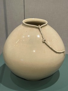 A round, white porcelain jar with a braided cord running out of the top of the jar.
