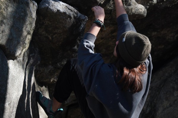A person wearing a gray beanie and gray sweatshirt climbs a rock.