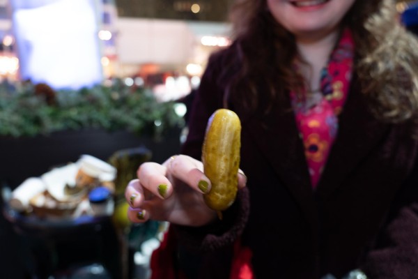 A person in a black coat holds out a green pickle.