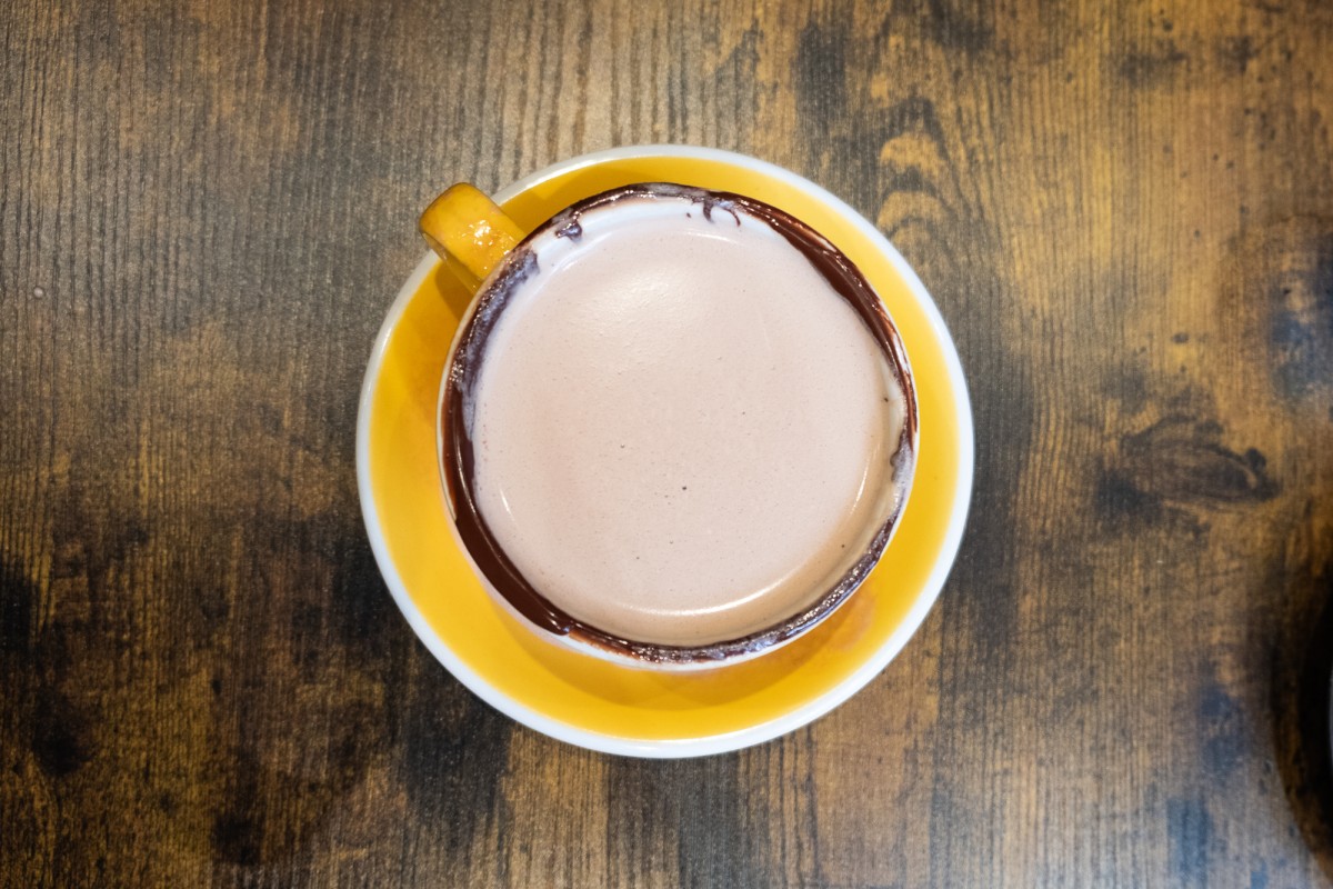 A yellow hot chocolate mug with a yellow plate underneath. It is on a wooden table.