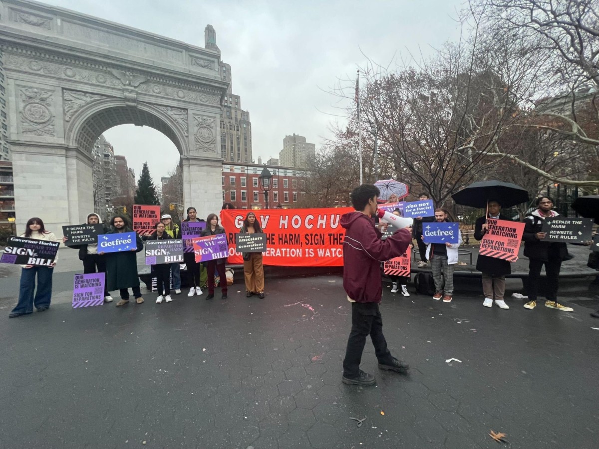 People holding various signs stand next to a large red banner with white and black text.