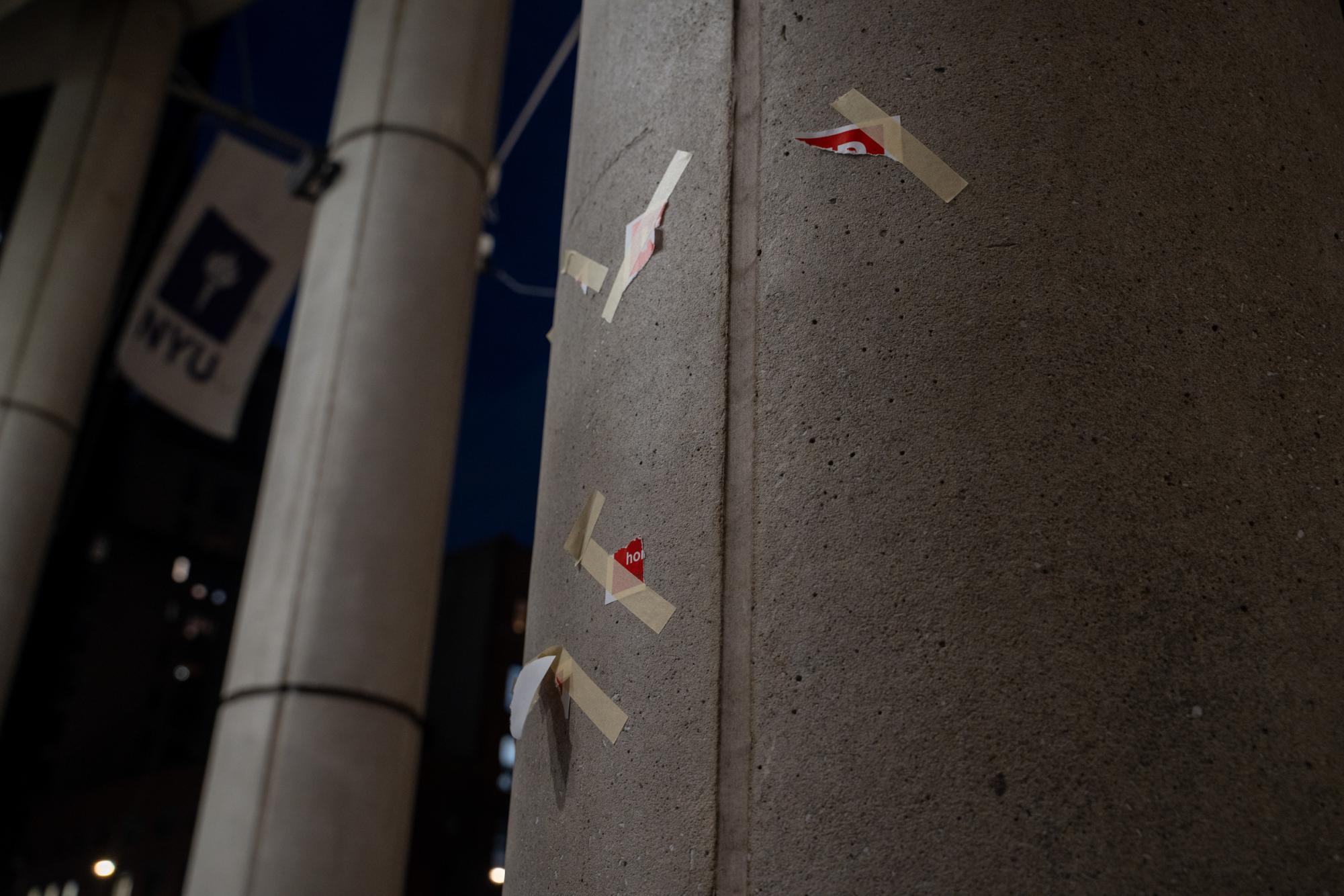 The remnants of a poster showing the Israeli hostages who are missing stuck on a pillar in N.Y.U.’s Stern School of Business. Behind the pillar is a white and purple N.Y.U. flag hanging on a building.