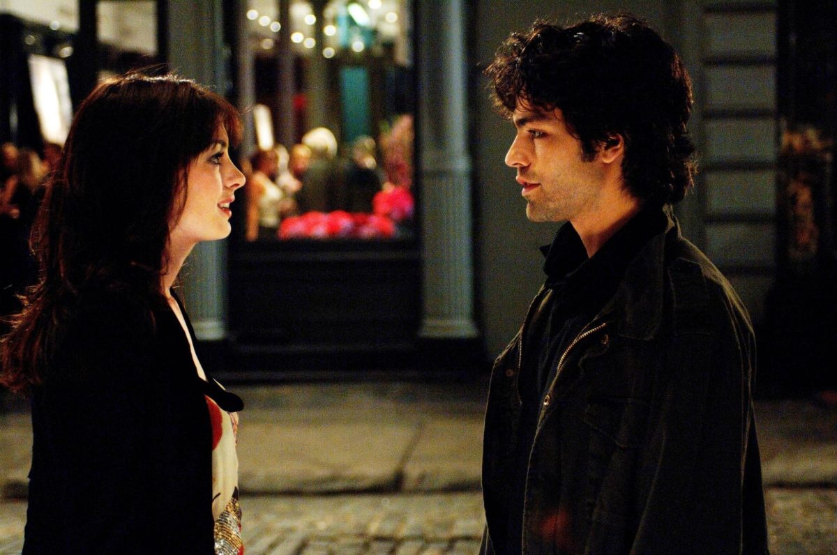 A man and woman standing face-to-face on a street at night time.