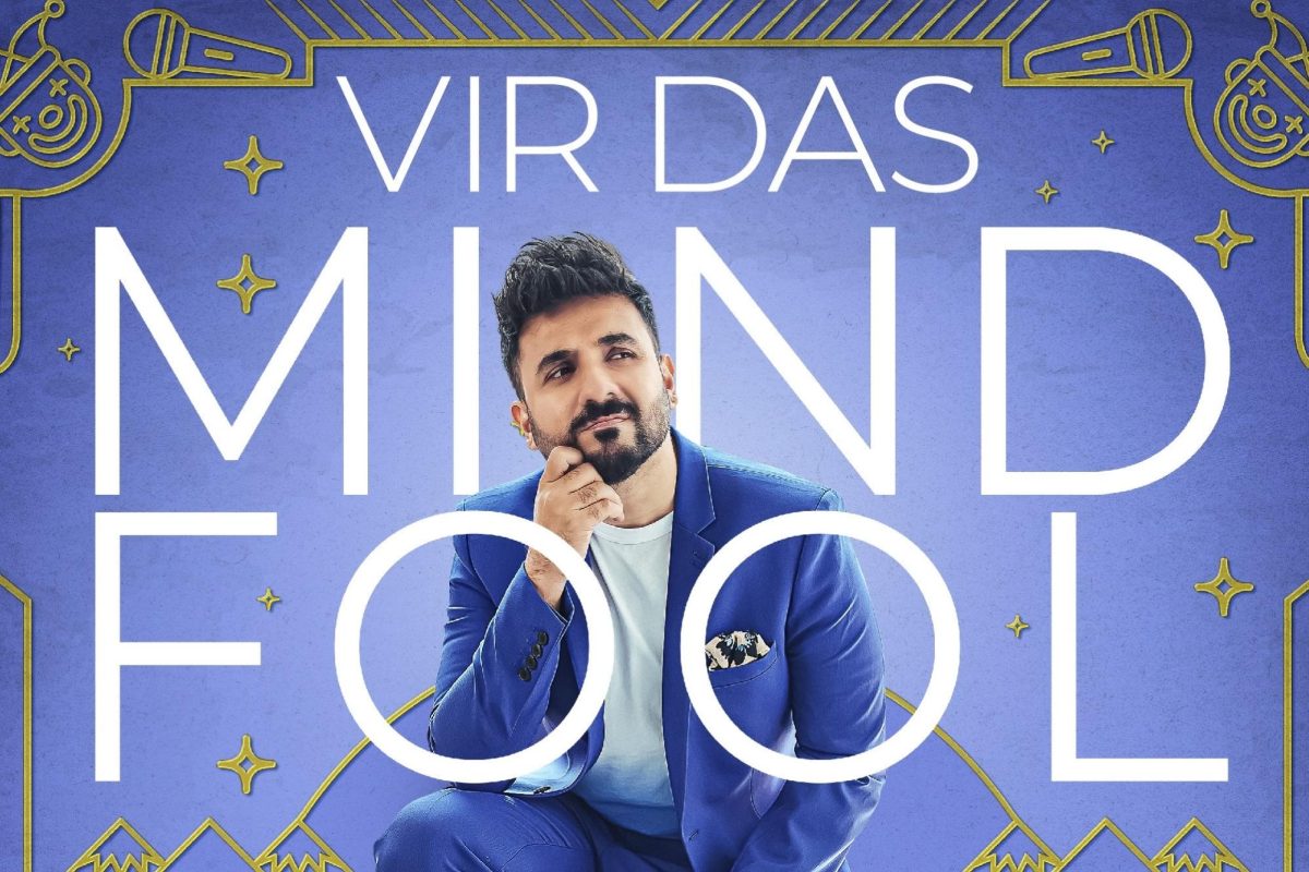 A bearded Indian man wearing a blue suit kneels between the white words “Vir Das Mind Fool.” There are gold designs depicting clowns, microphones and mountains bordering the frame.