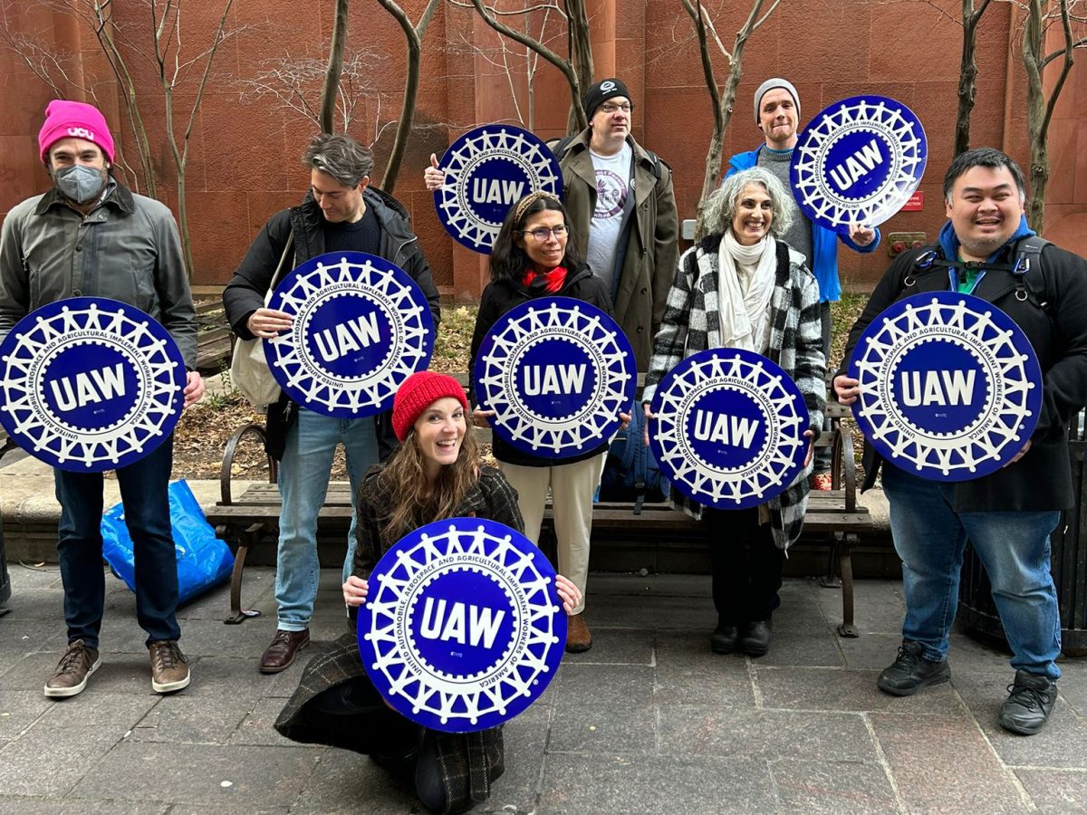 Eight+people+holding+circular+blue+signs+with+%E2%80%9CU.A.W.%E2%80%9D+printed+on+them+stand+outside+of+Bobst+Library.