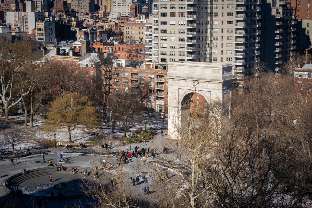 A bird’s eye view of Washington Square Park, with the trees barren and parts of the grass covered in snow. Dozens of people are walking in the square.