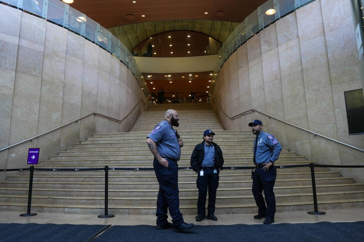 Three security guards in blue uniforms congregate in front of the Grand Staircase in the Kimmel Center for University Life. A barrier is placed both on the top and bottom of the staircase.
