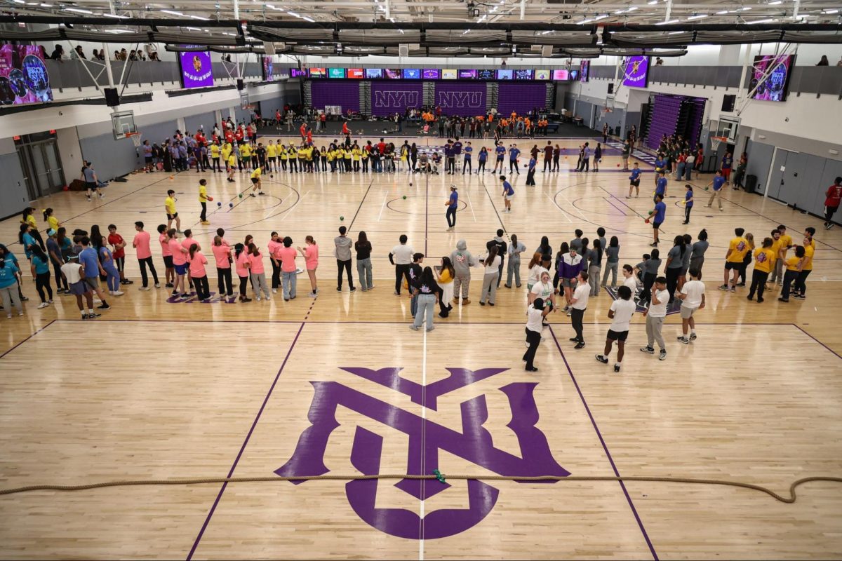 Groups of people stand between the basketball courts in the Paulson Center, with teams wearing matching colored shirts.