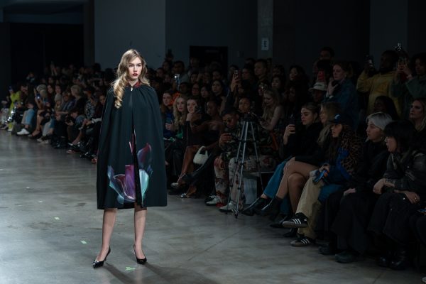A model walking down a runway with a black cape with a flower print.
