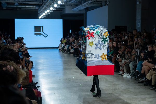 A model walking down a runway with an oversized blue-and-red hat with fabric flowers.