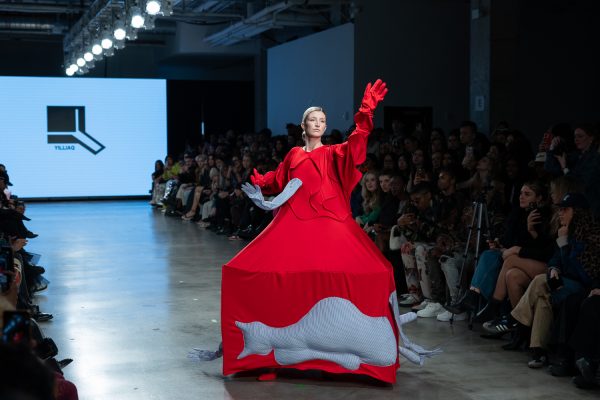 A model walking down a runway with a red dress that has a blue protruding hand and cat.