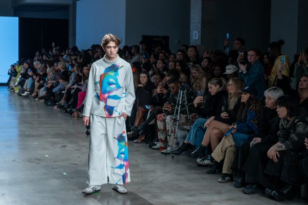 A model walking down a runway with a white shirt with a colorful splash print and matching pants.