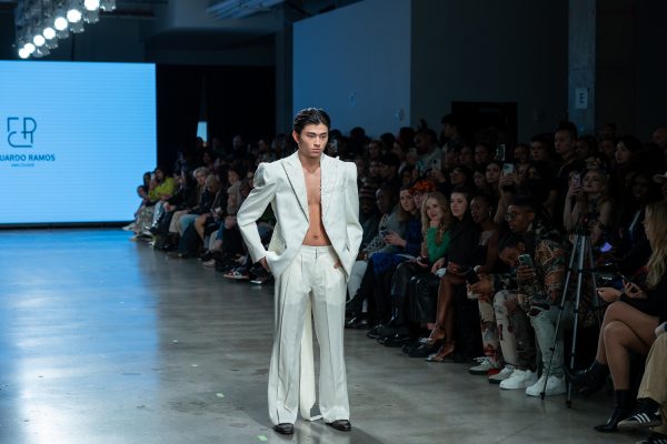 A model walking down a runway with a white blazer and slacks.