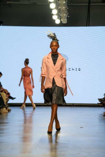 A model walking down a runway with a pink trench coat over a black dress.
