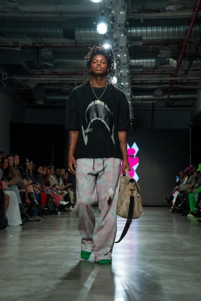 A model walking down a runway wearing a black t-shirt and floral sweatpants.