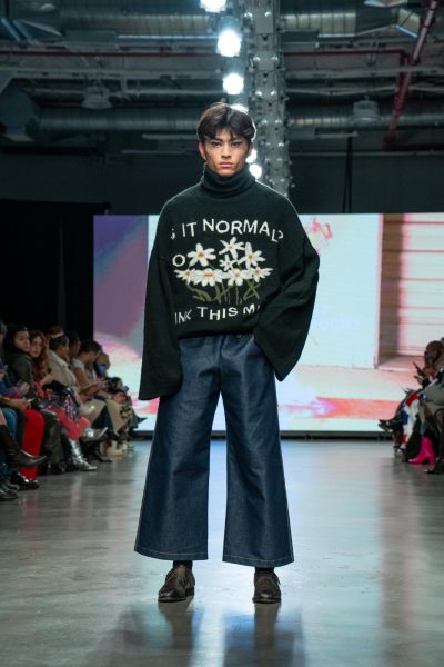A model wears a black turtleneck with white daisies that has white text on it and baggy blue jeans.