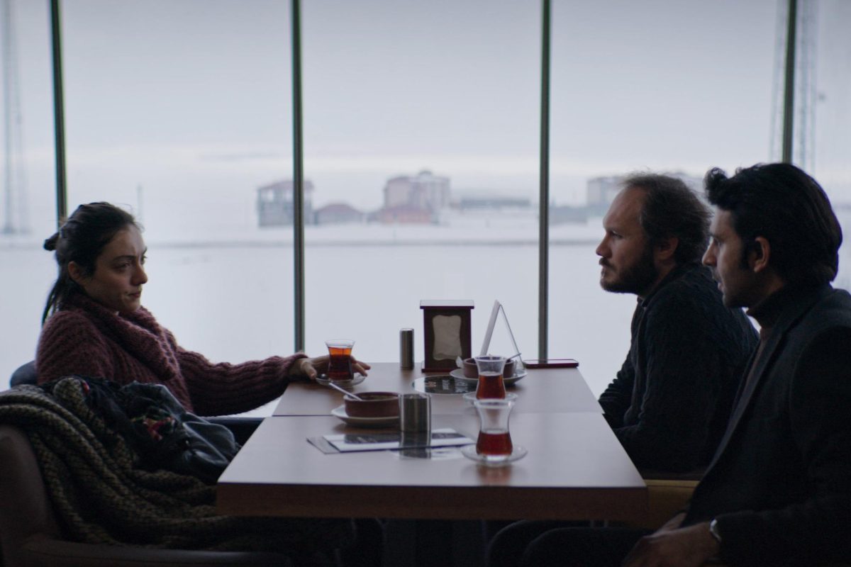 A woman sitting across from two men at a table with a snowy landscape in the background.