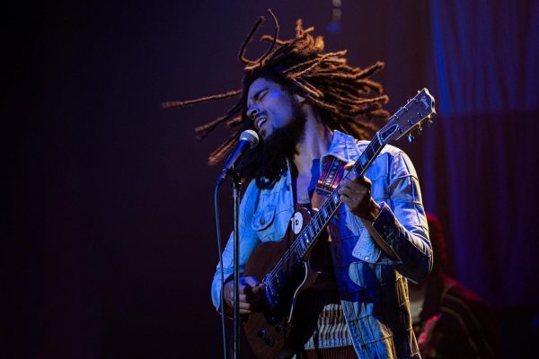 A man with dreads plays the guitar while singing into a microphone.