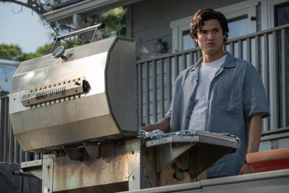 A man tending to a grill wearing a white shirt and blue button up.