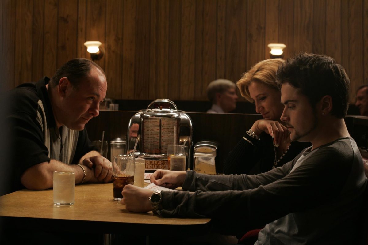 A man wearing a black, striped T-shirt across from a blonde woman and a man wearing a gray shirt and a watch in a diner booth.