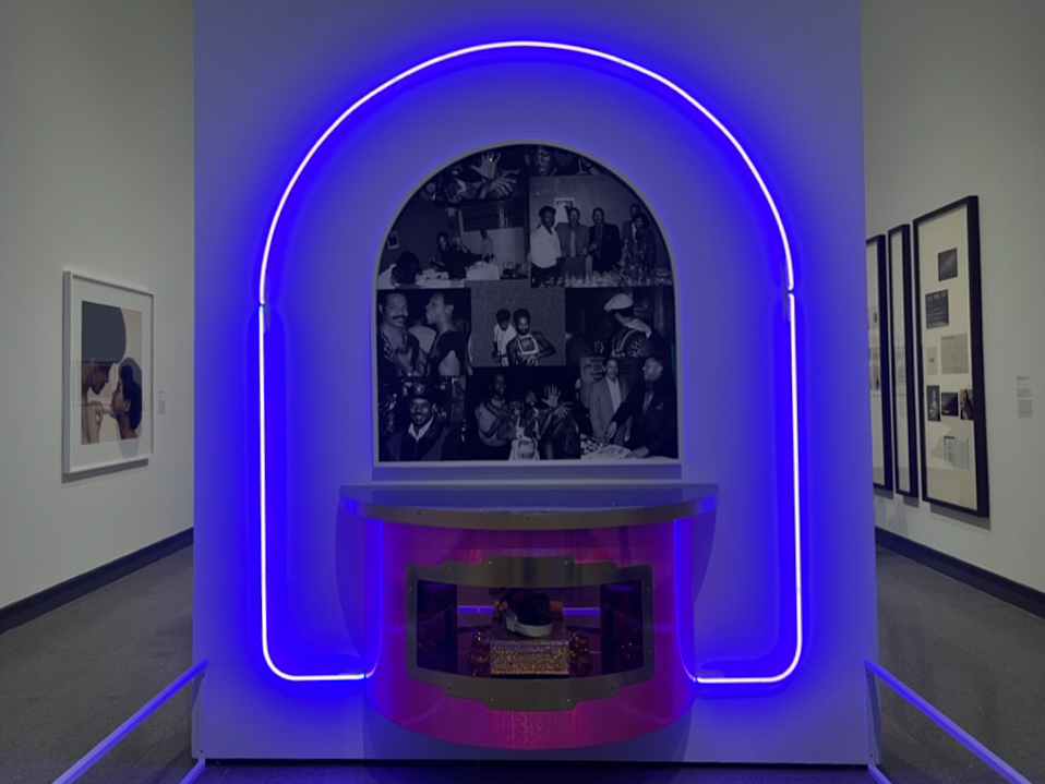 An arched purple neon light above a collection of black and white photos and a pink shelf.