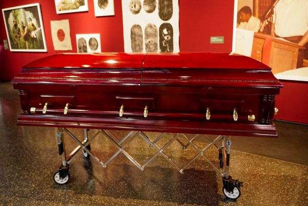 A red casket on a silver dolly in a gallery.