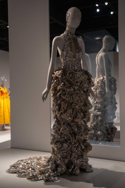 A mannequin wears an intricate ruffled dress made with small beads and a lace face covering.