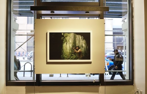 A photo of a man pointing a gun in a forest hangs in front of a window.