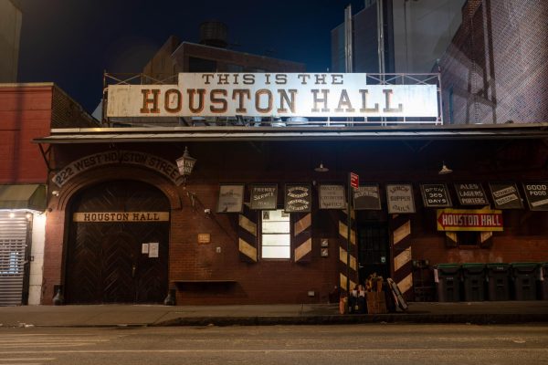 A brown western style building with the words "THIS IS THE HOUSTON HALL" on the top. There are multiple posters on the outer wall.