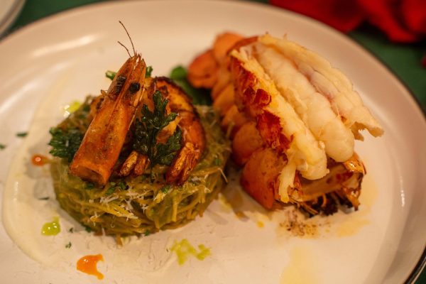 On the left of the plate, two prawns sit atop a green pesto pasta cake. On the right, there is lobster.