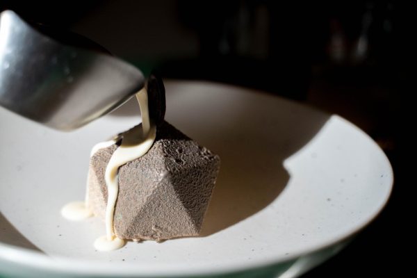 A white sauce is poured onto a gray geometric dessert.