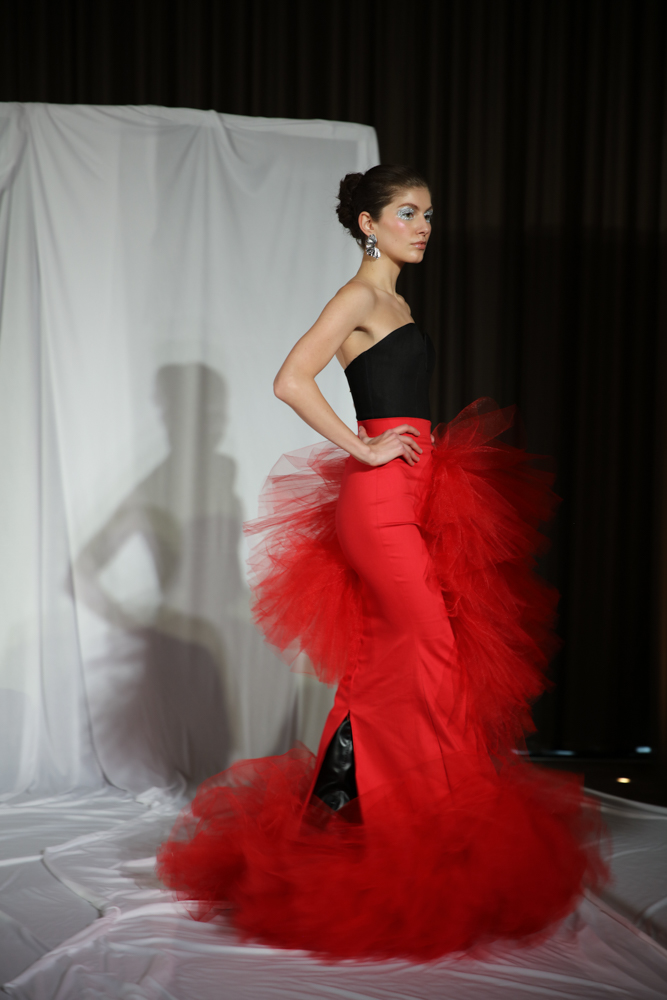 A model wearing a black and red dress with red tulle in front of a white backdrop.
