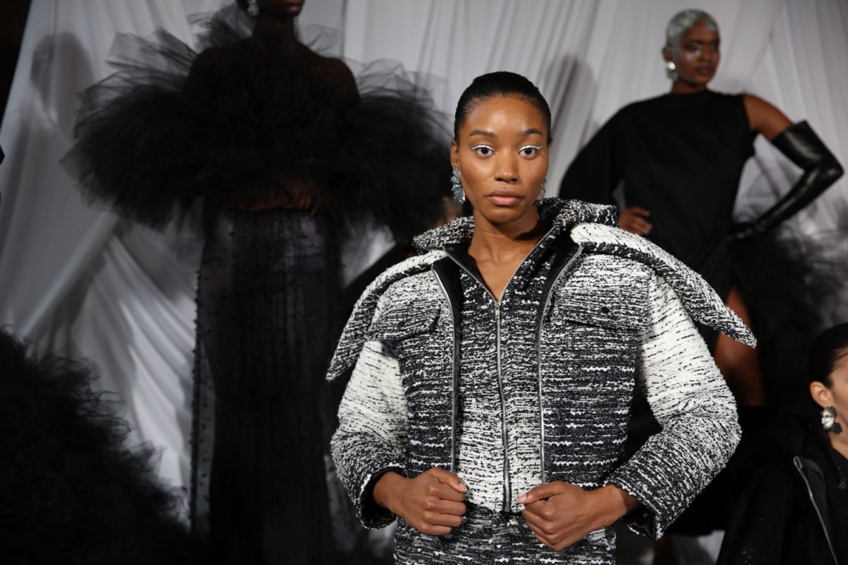A model wears a black-and-white patterned jacket with matching pants in front of other models.