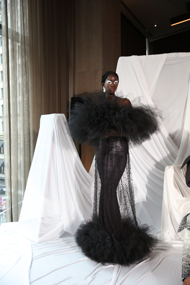 A model wears a black sheer dress with beaded details and black tulle at the top and bottom of the dress.