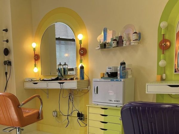 Orange and purple salon chairs are placed in front of two mirrors in a salon with green and yellow walls.
