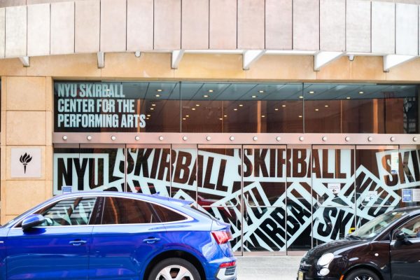Front entrance view of the Skirball Center, which includes the N.Y.U. logo and white graphics across the glass doors that read “SKIRBALL.”