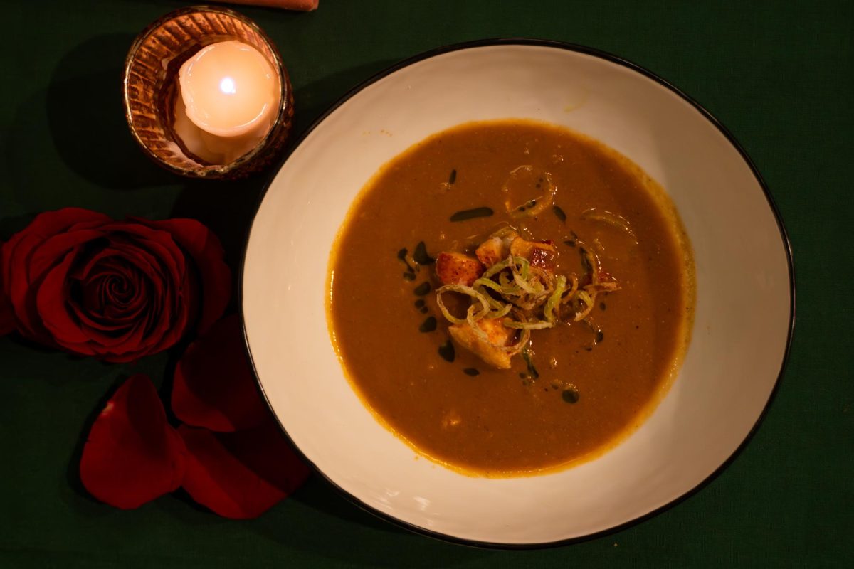 Aerial shot of orange soup with leeks. There is a candle and rose beside the dish.