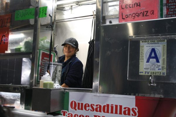 A woman smiles inside a silver food truck with signs on its exterior.