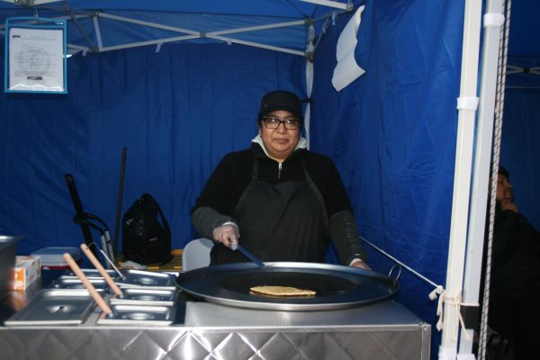 A woman cooking in a blue tent smiles.