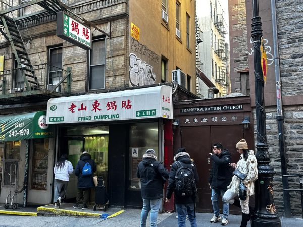 Several people stand outside of a restaurant which has a black and white exterior with red and green Chinese characters.