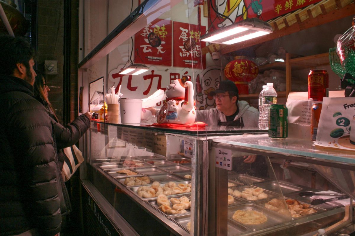 Two people order their food from an employee. On display are a variety of dumplings and other food. The restaurant is decorated with red lanterns, posters and a lucky cat.