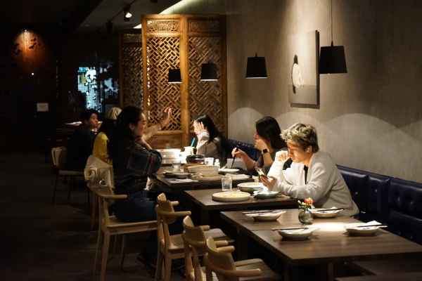 Several customers eating inside of Uluh, which has black leather booths and wooden tables and chairs.