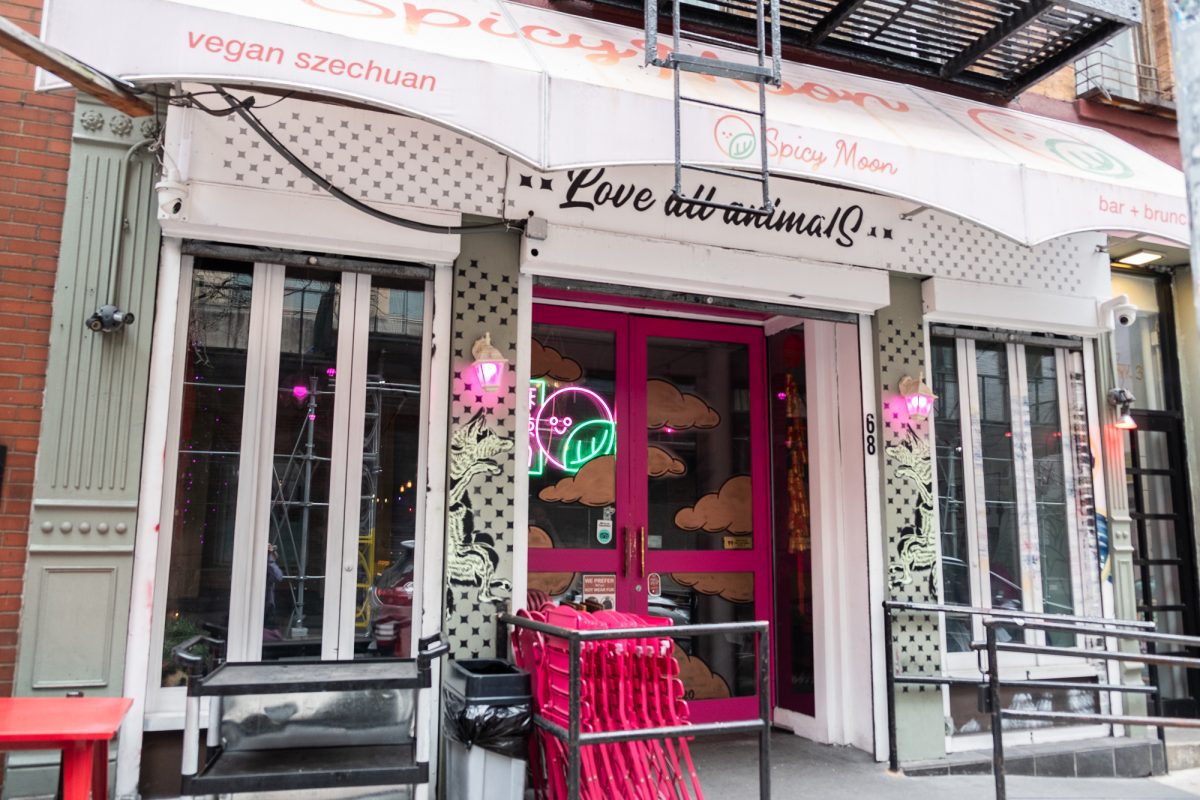 The pink-and-white storefront of a restaurant, with the words “Love All Animals” painted in black text above the door.